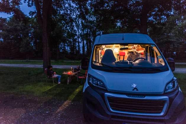 Camper sitzen zur blauen Stunde an einem lauen Sommerabend vor ihrem Camper auf Campingstühlen. Baden Württemberg, Deutschland. Mit einem Campervan unterwegs *** Campers sitting on camping chairs in front of their camper at blue hour on a warm summer evening Baden Württemberg, Germany On the road with a campervan