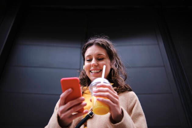 Smiling young woman with smoothie using smart phone near black door model released Symbolfoto ASGF00635