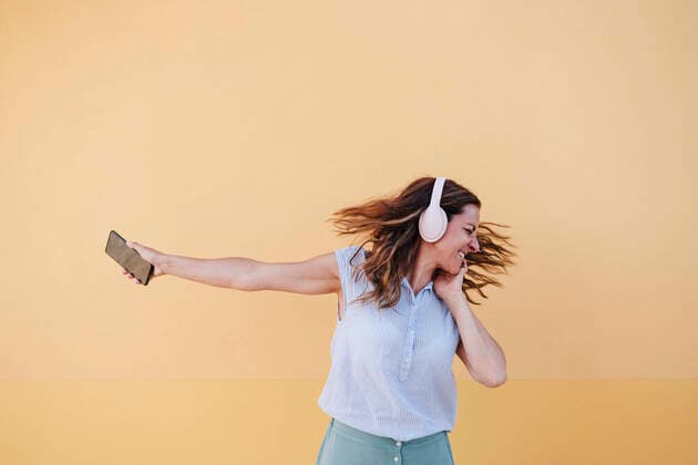 Cheerful woman with mobile phone listening music through headphones against wall model released Symbolfoto EBBF04183
