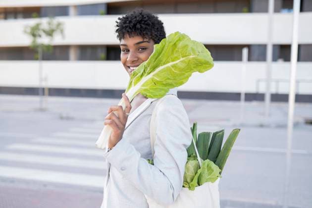 IMAGO Creative: Veganuary, fleischlos leben Smiling businesswoman holding leaf vegetable in city model released Symbolfoto JCCMF02921