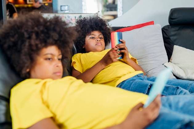 IMAGO Creative: Jahreszeit Winter, Couching Twin brothers using wireless technologies on sofa at home model released Symbolfoto property released MEUF03399