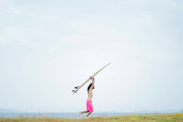 Carefree shirtless man carrying surfboard while running on meadow model released Symbolfoto property released PGF00620