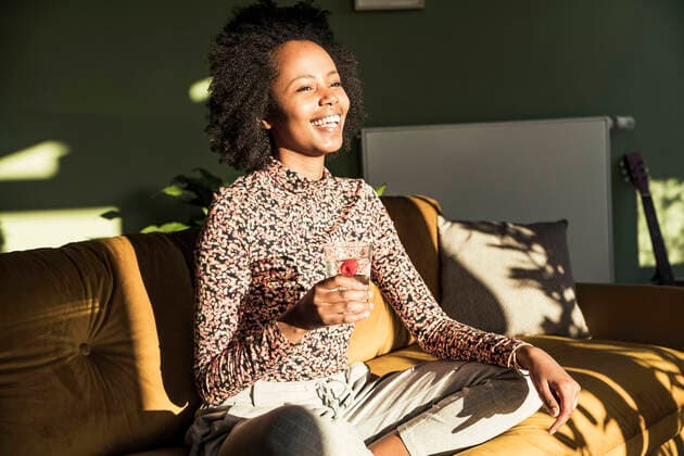 IMAGO Creative: Jahreszeit Winter, Couching Cheerful woman with drinking glass looking away while sitting on sofa model released Symbolfoto property released UUF23613