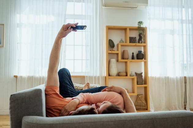 IMAGO Creative: Jahreszeit Winter, Couching Man embracing woman while taking selfie through mobile phone at home model released Symbolfoto property released VPIF04363