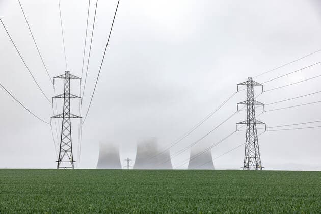 UK, England, Rugeley, Electricity pylons standing in field during foggy weather with cooling towers in background WPEF04930
