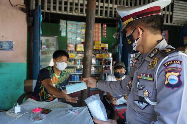 Indonesia: Sharing Aid during pandemic Personnel of the Traffic Directorate of the South Sulawesi Police gave free masks to a resident at Mallengkeri Terminal, Makassar City, Indonesia, during the implementation of Level IV Community Activity Restrictions (PPKM), to prevent the spread of Covid-19 Makassar South Sulawesi Indonesia Copyright: HerwinxBahar