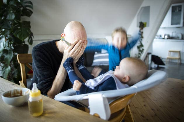 IMAGO Creative, Gesellschaft, Immer mehr Menschen haben Angst vor der Zukunft Symbolfoto: Ein Vater haelt sich verzweifelt die Hande vor das Gesicht weaehrend er sein Baby fuettert und ein weiteres Kind wuetend im Hintergrund herumspringt. Berlin, 02.02.2021. Berlin Deutschland *** Symbolic photo A father desperately holds his hands in front of his face while he feeds his baby and another child jumps around in the background crying Berlin, 02 02 2021 Berlin Germany Copyright: xJaninexSchmitz photothek.dex