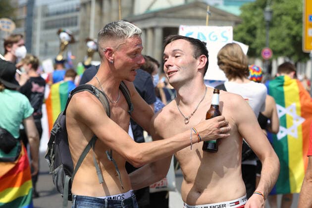 Berliner CHRISTOPHER STREET DAY 2021 - CSD - Am 24. Juli 2021 zieht der CSD in Berlin unter dem Motto SAVE OUR COMMUNITY SAVE YOUR PRIDE zum 43. Mal durch die Hauptstadt. Zwei junge Männer mit freiem Oberkörper im Bereich des Brandenburger Tores. Rechts im Bild: Regenbogenflagge mit Davidstern. Die bunte CSD-Parade startete in diesem Jahr als Demonstration an der Leipziger Straße, führte über den Potsdamer Platz, vorbei am Denkmal für die im Nationalsozialismus verfolgten Homosexuellen zum Brandenburger Tor und über die Siegessäule zur Urania. Aufgrund der Corona-Pandemie fand die Demonstration ausschließlich unter Einhaltung der vom Berliner Senat erlassenen Vorgaben statt. Die in den Vorjahren übliche Abschlusskundgebung mu