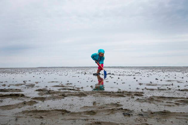 Girl playing in mud flat with shovel against sky at Lower Saxon Wadden Sea National Park, Germany model released Symbolfoto LHF00824