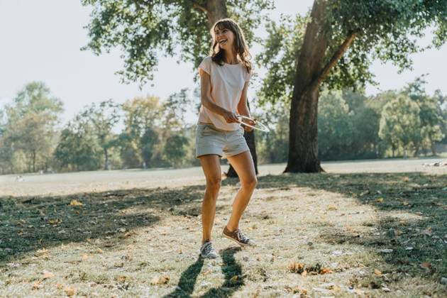 Mature woman throwing frisbee ring while standing in public park on sunny day model released Symbolfoto MFF06409