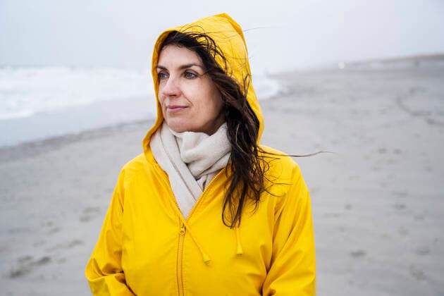 IMAGO Creative: Internationaler Frauenmonat, Gesundheit, Frauen in der Menopause Contemplated mature woman in yellow raincoat at beach during weekend model released Symbolfoto UUF22044