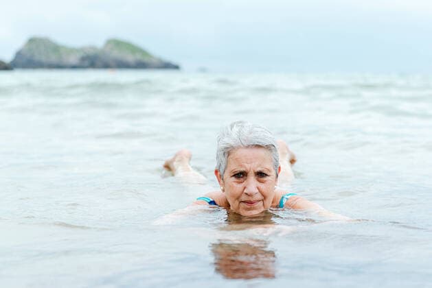 IMAGO Creative: Sommer Sport - Strand Active senior gray haired female swimming in ocean water while enjoying summertime and practicing healthy lifestyle on seashore, Model released AlbertoMenendez_OldWomanBeach_25.jpg Copyright: xAlbertoxMenendezx MR