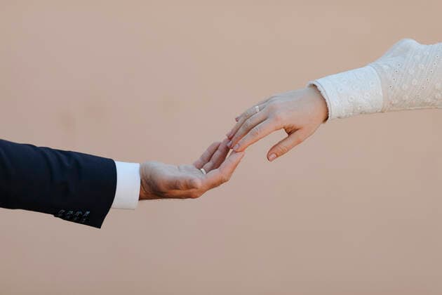 Crop anonymous romantic newlywed couple in elegant classy wedding clothes with engagement rings touching hands gently against beige background AlbertoOrtega_WeddingDetails_25.jpg Copyright: xAlbertoxOrtegax Model Released