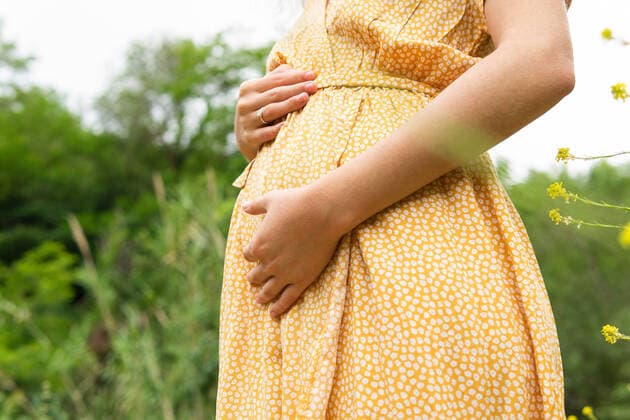 Side view of crop anonymous pregnant female in summer dress touching tummy while standing in field in countryside, Model released DavidMunoz_LuciaPark_13.jpg Copyright: xDavidxMunozx MR