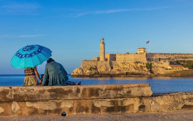 HAVANA, CUBA - JANUARY 2. 2021: El Morro Lighthouse from the Malecon in Havana, Cuba Couple sitting at the Malecon witg blue umbrella looking at the El Morro. Havanna Cuba *** HAVANA, KUBA 2. JANUAR 2021 El Morro Leuchtturm vom Malecon in Havanna, Kuba Paar sitzt am Malecon mit blauem Schirm und schaut auf den El Morro Havanna Kuba Copyright: xChristianxOffenbergx