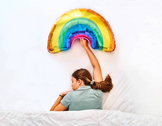 Creative Highlights Symbolbilder Top view of young female holding multicolored rainbow inflatable balloon while sleeping under blanket in bed with white sheets AdalbertoRodriguez_StudentAtHome_1.jpg Copyright: xAdalbertoxRodriguezx Model Released