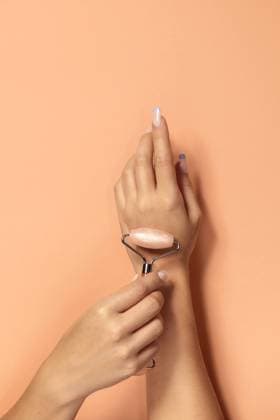Creative Highlights Symbolbilder Crop anonymous female demonstrating pink quartz roller for facial skin treatment and massage against beige background, Model released AdrianSava_Hands_15.jpg Copyright: xAdrianxSavax MR