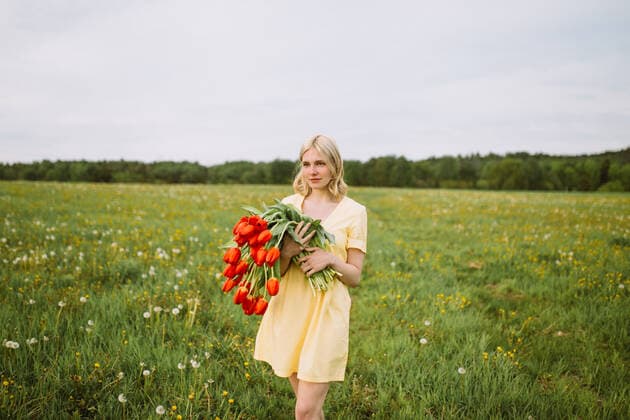 Content female in dress standing with bunch of red tulip flowers in meadow in summer and looking away CamilleGirard_GirlWithTulips_30.jpg Copyright: xCamillexGirardx Model Released