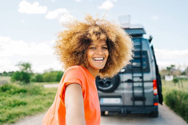 Creative Highlights Symbolbilder Happy African American woman with longboard smiling and looking at camera while leading crop friend to van during road trip, Model released, Property released JakeJakab_AfroWomanInNature_77.jpg Copyright: xJakexJakabx MR