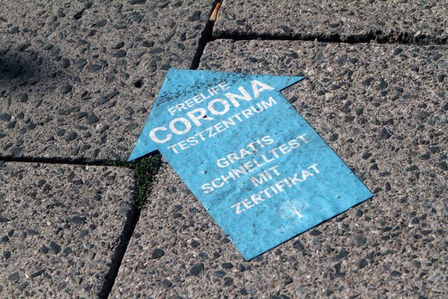 Aufkleber mit Richtungspfeil und Aufschrift Freelife Corona Testzentrum gratis Schnelltest mit Zertifikat klebt auf einem Gehweg in der Innenstadt von München, Bayern, Deutschland