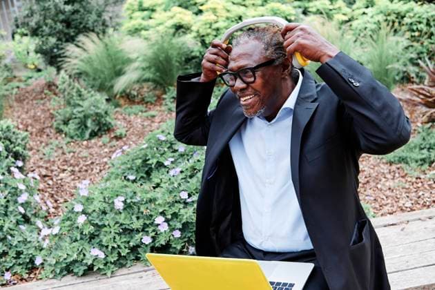 IMAGO Creative: Klimawandel - Zukunft und Innovation Smiling businessman wearing headphones while sitting with laptop on bench model released Symbolfoto ASGF00926