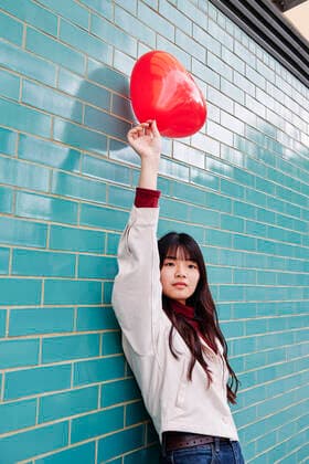 Beautiful woman holding red balloon while leaning on turquoise brick wall model released Symbolfoto ASGF00946