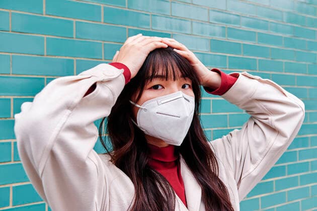 Woman with head in hands wearing protective face mask during pandemic model released Symbolfoto ASGF00959