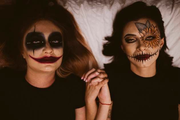 Female friends with evil make-up holding hands while lying on bed model released Symbolfoto EGHF00125