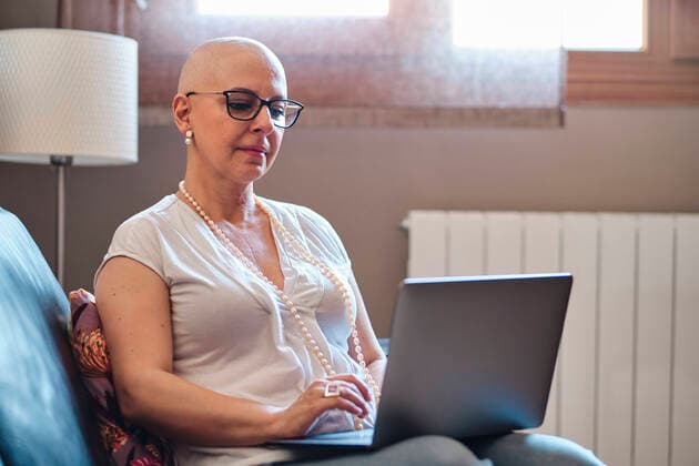 IMAGO Creative: Brustkrebsmonat Bald woman using laptop in living room at home model released Symbolfoto property released AGOF00197