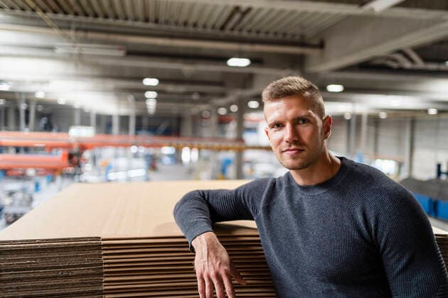 IMAGO Creative: Business, Inflation und Lieferketten Young businessman staring while leaning on cardboard stack model released Symbolfoto property released DIGF16209