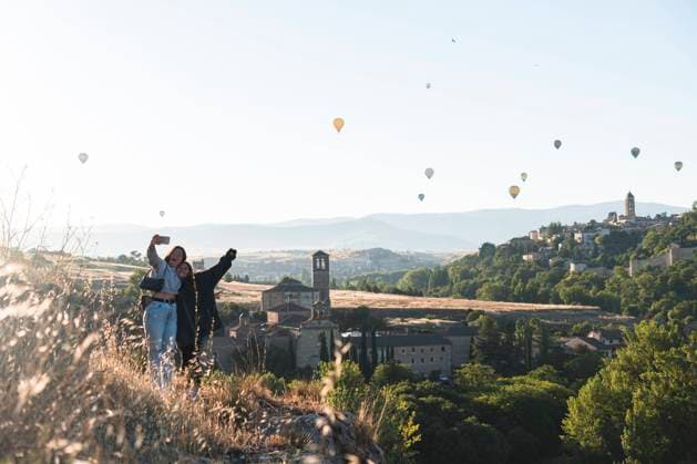 IMAGO Creative, Jahreszeit Sommer, Sommer in der Stadt Spain, Castile and Leon, Segovia, Two sisters taking selfie with flying hot air balloons and historical city buildings model released Symbolfoto JAQF00693