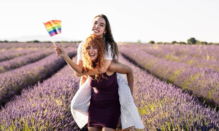 Happy girlfriends with LGBTQIA Flag in lavender field model released Symbolfoto JCCMF03186