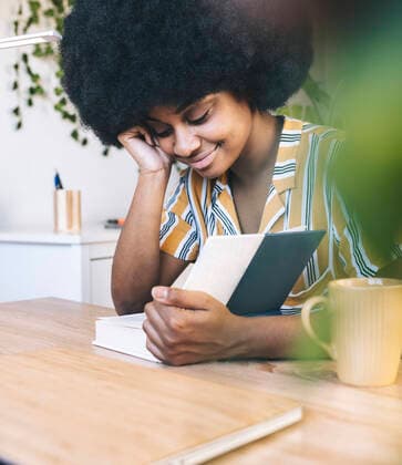 Afro woman reading book at desk model released Symbolfoto property released JCCMF03316