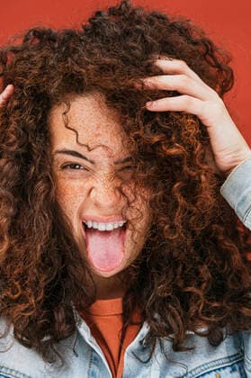 Young curly haired woman with hands in hair sticking out tongue model released Symbolfoto JCMF02098