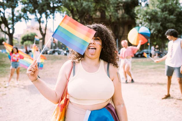 Young woman holding rainbow flag while friends in background at park model released Symbolfoto MEUF03621