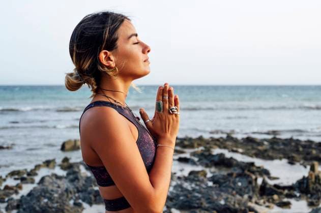 Young woman with hands clasped meditating at beach model released Symbolfoto PGF00717