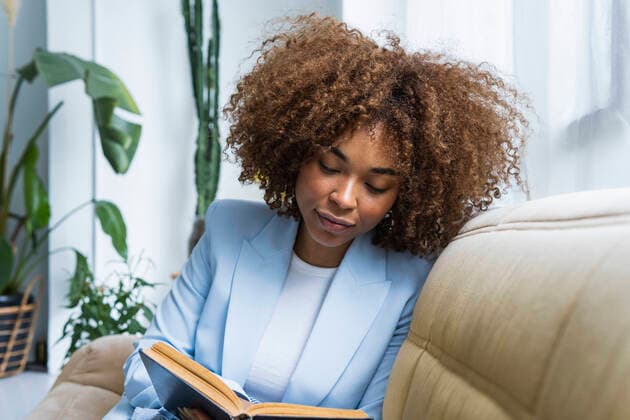 Young businesswoman reading book while sitting on sofa in living room model released Symbolfoto property released PNAF02103
