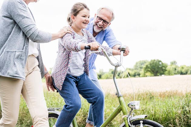 Granddaughter practicing bicycle with grandparents at meadow model released Symbolfoto UUF24159