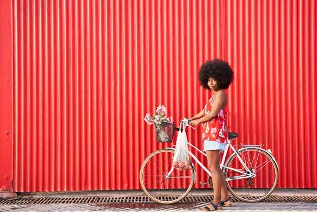 Afro woman with bicycle standing by red corrugated wall model released Symbolfoto VEGF04808