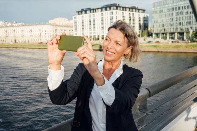 IMAGO Creative: Internationaler Frauenmonat, Gesundheit, Frauen in der Menopause Mature businesswoman photographing through mobile phone by railing in city model released Symbolfoto VPIF04489