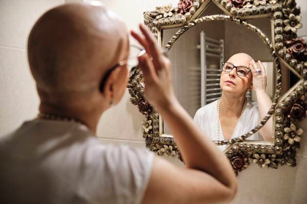 IMAGO Creative: Brustkrebsmonat Woman with cancer touching bald head while looking at reflection in mirror model released Symbolfoto property released AGOF00201