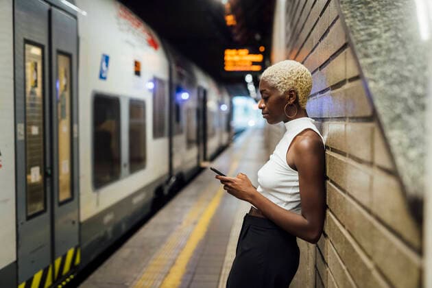 IMAGO Creative: Ruhe im Chaos Woman using mobile phone while leaning on wall at subway station model released Symbolfoto MEUF04016