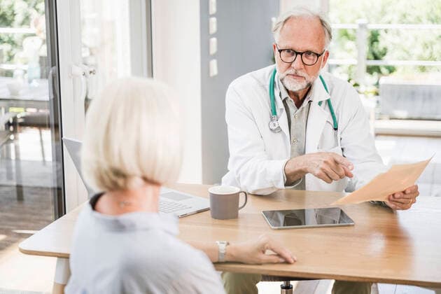 IMAGO Creative: Brustkrebsmonat Male doctor holding medical report while looking at female patient at desk model released Symbolfoto property released UUF24061