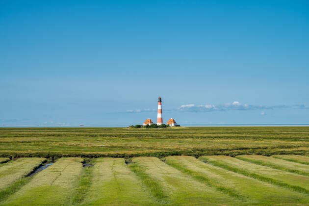 August 2021 Eiderstedt, Schleswig-Holstein Wanderung um den Leuchtturm von WesterheverNordseeküste Westerhever Leuchtturm mit grünen Salzwiesen, ein Fischkutter passiert im Hintergrund *** August 2021 Eiderstedt, Schleswig Holstein Hiking around the lighthouse of WesterheverNorth Sea coast Westerhever lighthouse with green salt marshes, a fishing boat passes in the background