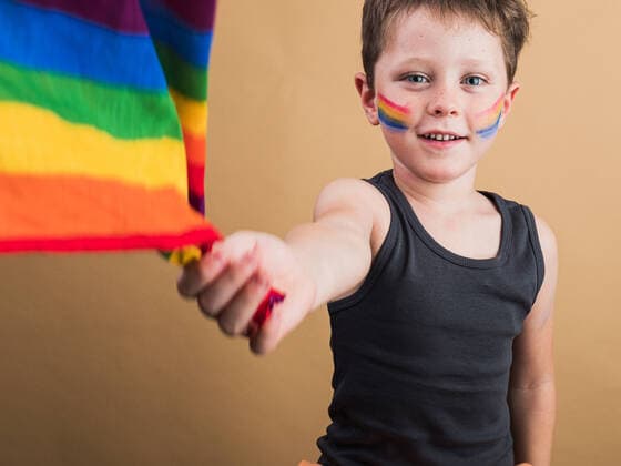 IMAGO Creative: Pride Month 2022, Engagement der Jugendlichen Cheerful kid with makeup on cheeks with LGBTQ flag while looking at camera on beige background HodeiUnzueta_EtxahumStudioConcepts_59.jpg Copyright: xHodeixUnzuetax Model Released