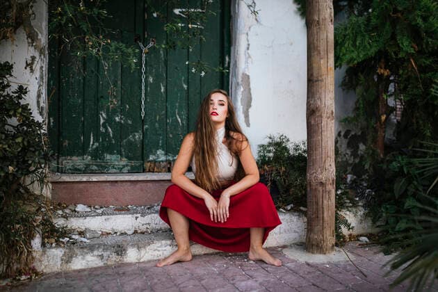 Side view of charming woman in skirt and crop top sitting on stone steps in patio with green plants and looking at camera, Model released, Property released PabloGallardo_CasaPatio_15.jpg Copyright: xPabloxGallardox MR