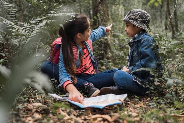 IMAGO Creative: Klimawandel - Umwelterziehung Ethnic girl showing green plant to brother while looking away and sitting on terrain with paper map and loupe in woods, Model released ReneStevens_ExplorerKids_58.jpg Copyright: xRenexStevensx MR