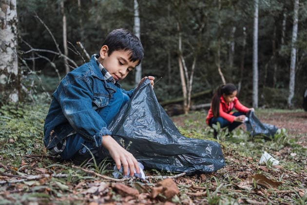 IMAGO Creative: Klimawandel - Umwelterziehung Ethnic volunteers with plastic bags picking rubbish from terrain against trees in summer woods in daylight, Model released ReneStevens_ExplorerKids_80.jpg Copyright: xRenexStevensx MR