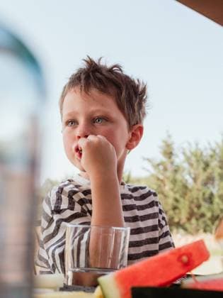 IMAGO Creative: Clickbait, Rezepte und Kochen Low angle of cute little child sitting at table in courtyard in summer and eating fresh sweet watermelon while looking away, Model released, Property released HodeiUnzueta_OllerDelMas_30.jpg Copyright: xHodeixUnzuetax MR