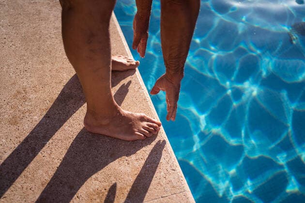 High angle of crop anonymous barefoot person stretching forward while standing on poolside edge near clean water, Model released JuanAlbertoRuiz_FamilyAtPool_148.jpg Copyright: xJuanxAlbertoxRuizx MR